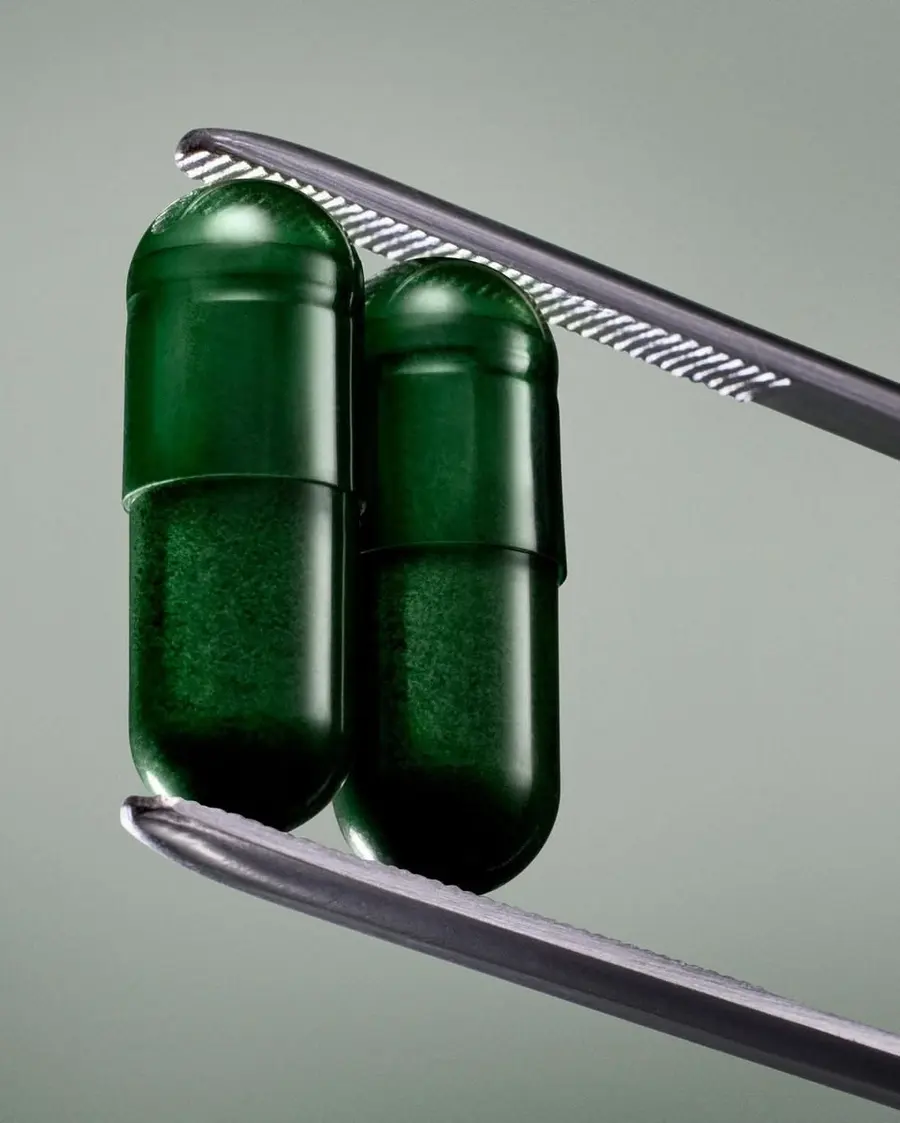 Dos cápsulas verdes sostenidas con pinzas de precisión
